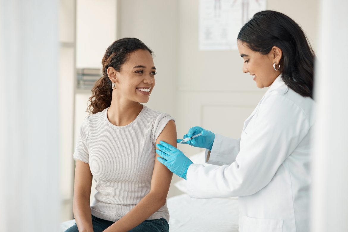 shot of an attractive young doctor standing and injecting her patient during a consultation in the clinic