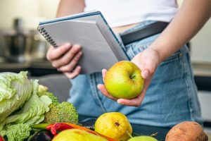 woman with notepad vegetables kitchen table preparing recipe